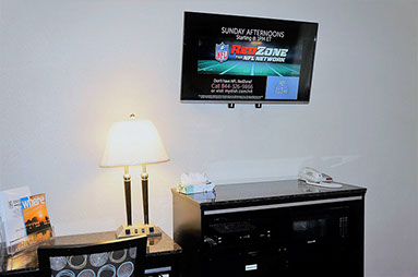 PHoto showing large flat screen television, chest of drawers with an accessible writing table, chair and lamp. Dial direct phone in room.