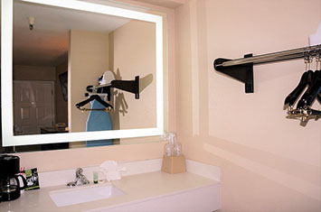 Guest bathroom showing vanity with mirror, coffee maker, ironing board and iron. Shelf with hangers for your clothes